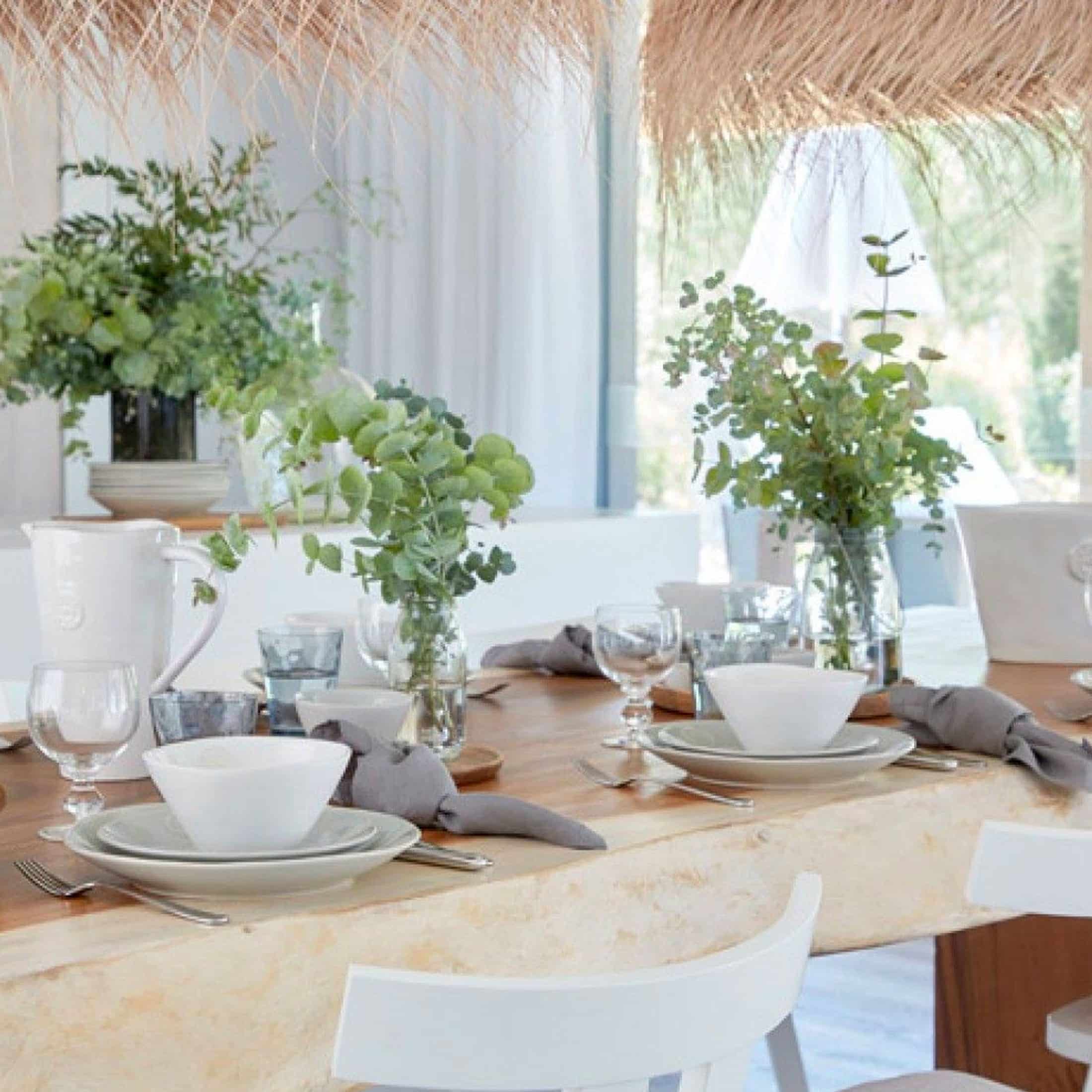 Weißes Geschirr der Serie Costa Nova Nova mit dem charakteristischen runden Siegel-Logo auf einem mediterranen Tisch.