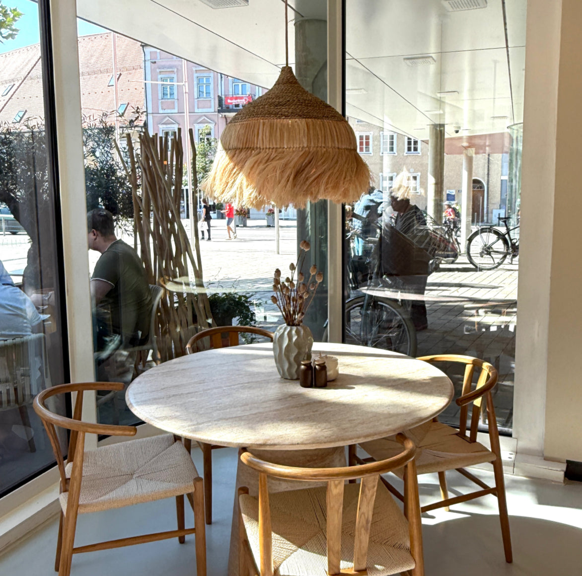 Boho Rattan-Hängelampe über einem runden Tisch in einem hellen Café