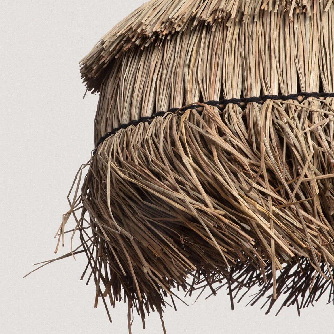 Detailaufnahme der Unterseite der Rattan Pendelleuchte Liana mit natürlichen Fransen aus Rattan im Boho Stil, die warmes Licht weich im Raum streuen.