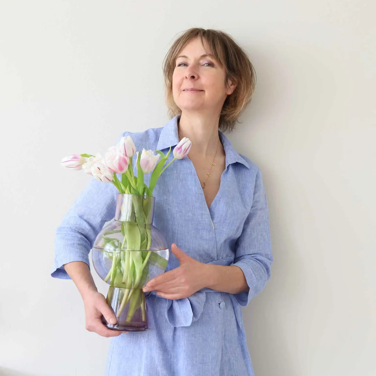 Gründerin von Soulbirdee mit Tulpenstrauß und Glasvase vor heller Wand