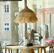 hängelampe groß 60 cm rund mit Fransen aus Gras im Boho Style über einem runden Tisch in einem cafe