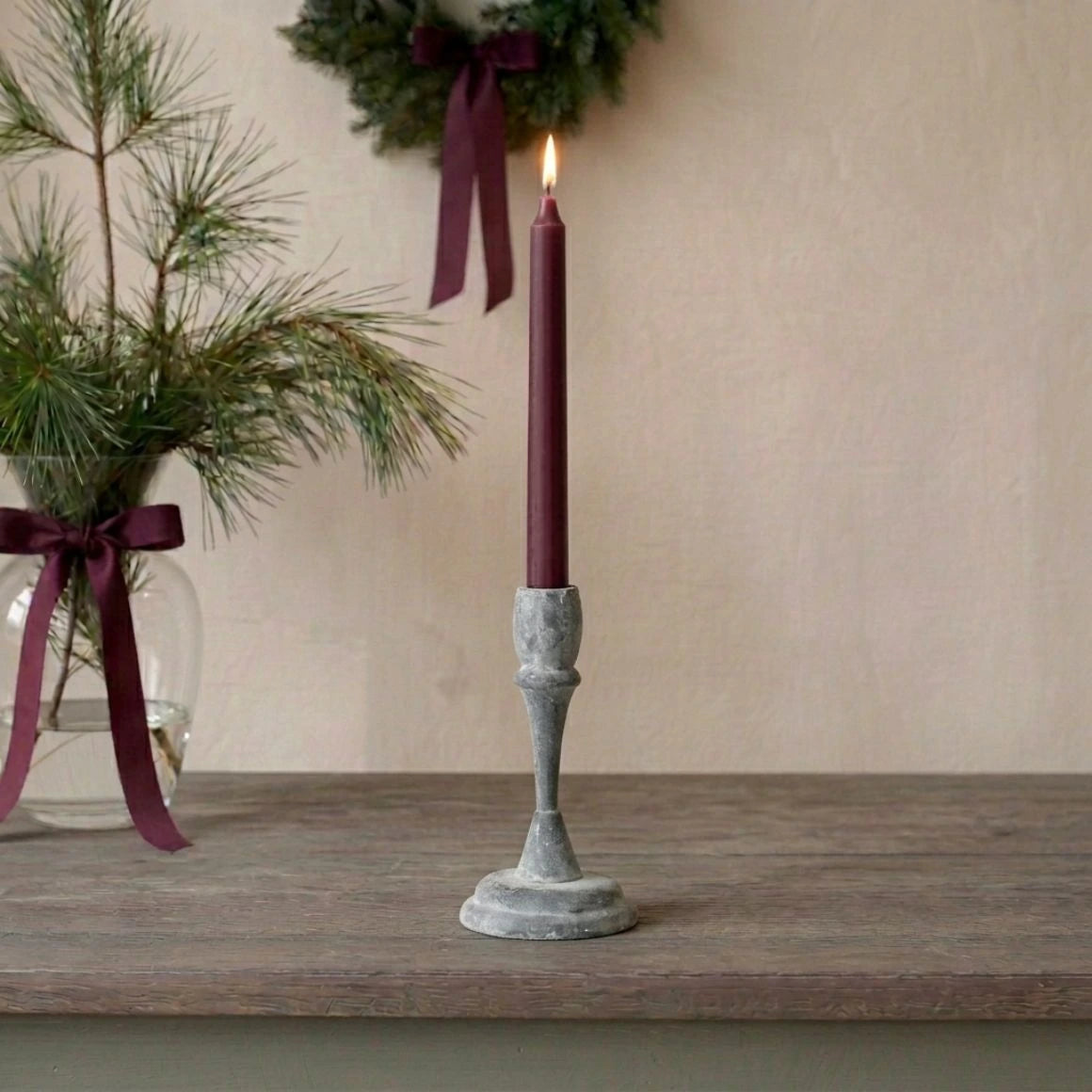Grauer Kerzenständer Rosie Mini aus Eisen von Affari of Sweden, 18 cm hoch, mit bordeauxroter Stabkerze auf rustikalem Holztisch im skandinavischen Landhausstil.