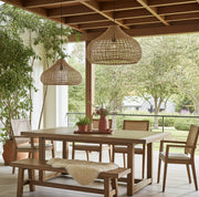 Große Outdoor Rattan Pendelleuchte Mira in 2 Größen über Holztisch auf überdachter Terrasse – moderne Outdoor-Beleuchtung.