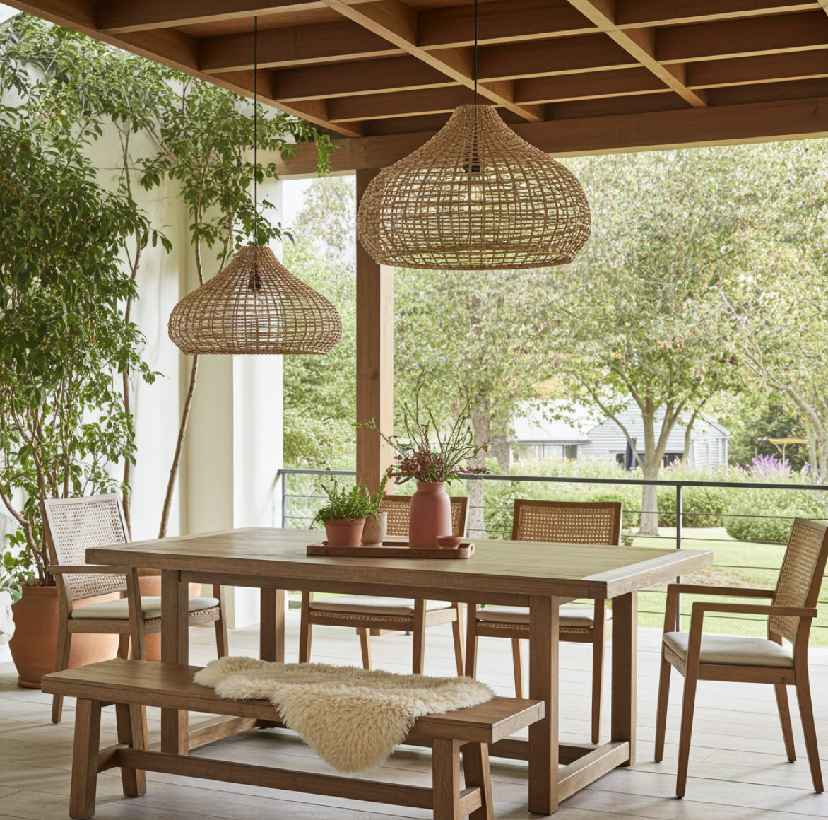 Große Outdoor Rattan Pendelleuchte Mira in 2 Größen über Holztisch auf überdachter Terrasse – moderne Outdoor-Beleuchtung.