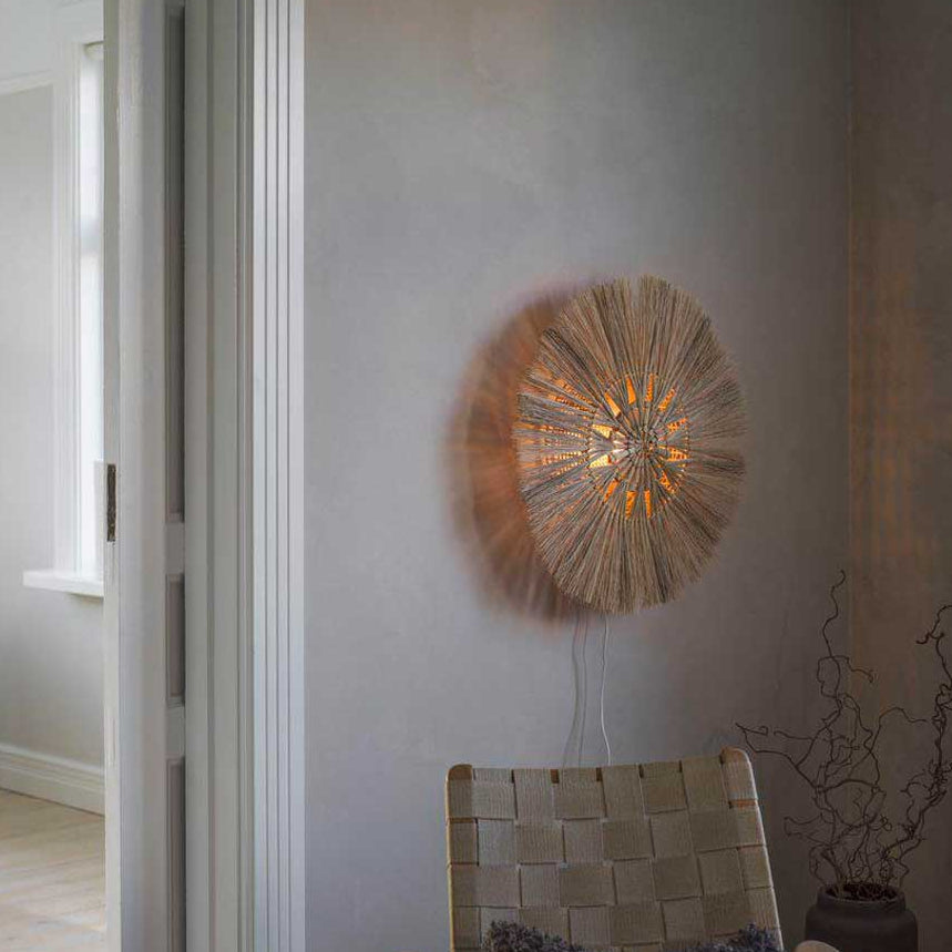 Runde Wandlampe aus Naturmaterial mit warmem Licht an heller Wand