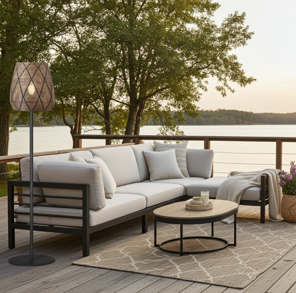 Moderne Terrassenlampe oder Stehampe mit Rattan Lampenschirm und schwarzem Fuss steht auf einer Terrasse mit Holzboden neben einem modernen Sofa